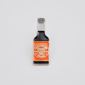 small black and orange enamel pin in the shape of a henderson's relish bottle